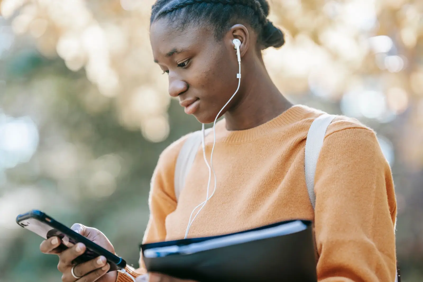 A young woman with earphones looking at her phone outdoors