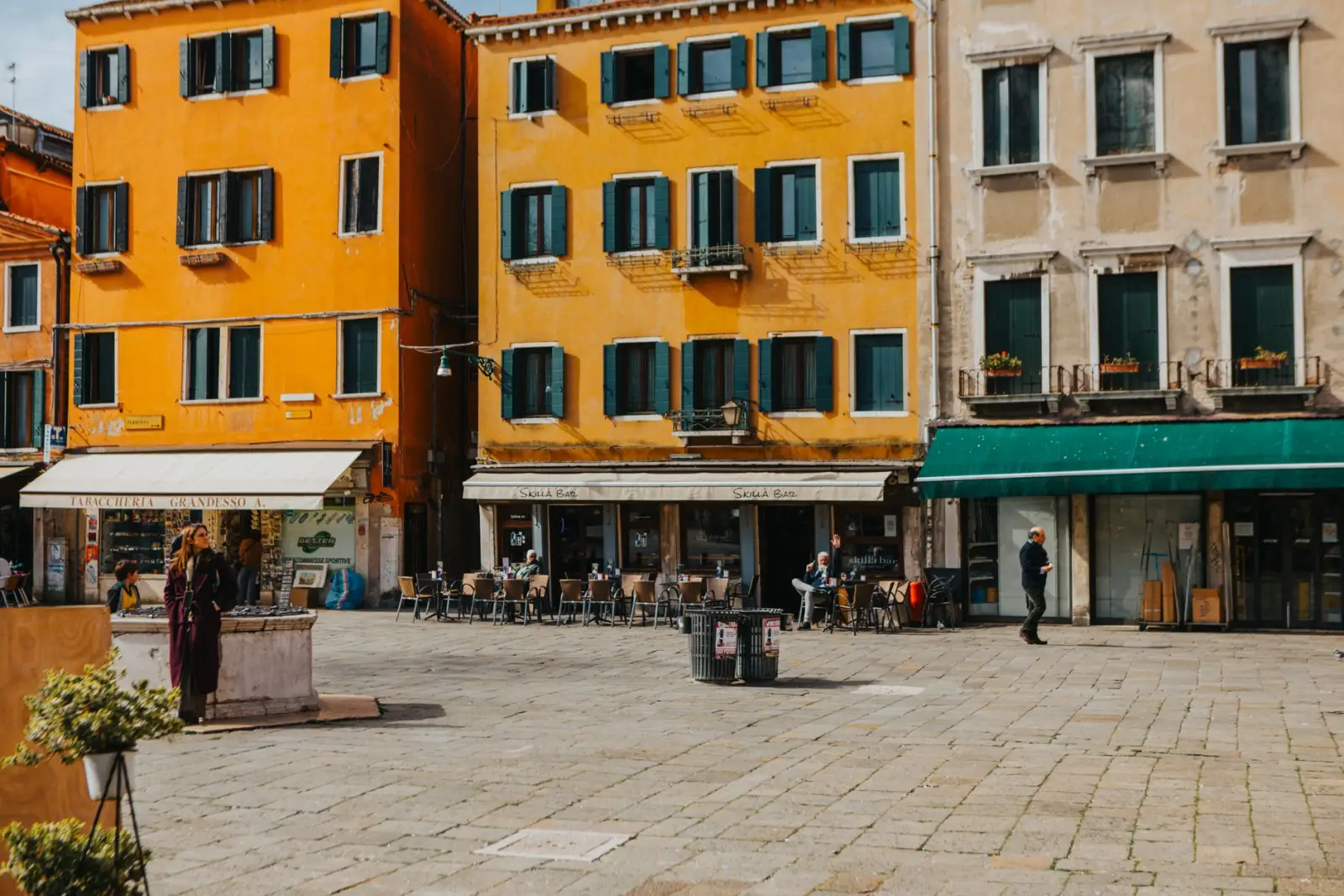 A Venetian square with orange and yellow houses and people at outdoor café tables